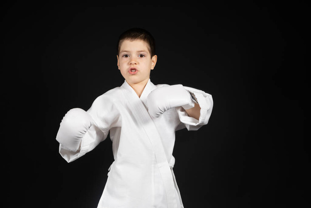 Een kleine jongen leert martial arts, karate doen in kimono en bokshandschoenen handpads - Foto, afbeelding