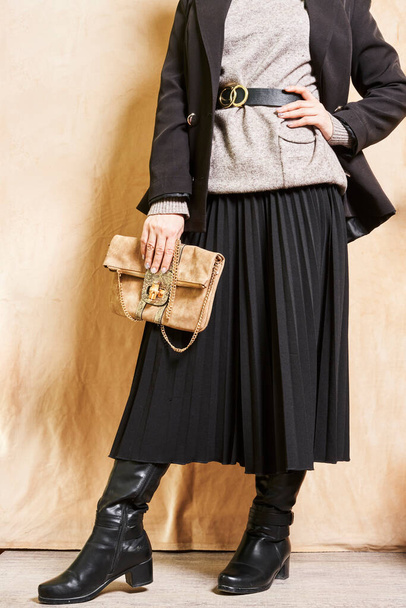 Siyah bir ceket giyen ve sağ elinde kahverengi bir çanta tutan bir kadın bej bir duvarın önünde dikiliyordu. - Fotoğraf, Görsel
