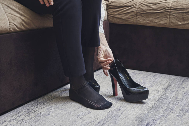 una donna gambe e scarpe sedute sul pavimento di fronte a un divano con i piedi appoggiati - Foto, immagini