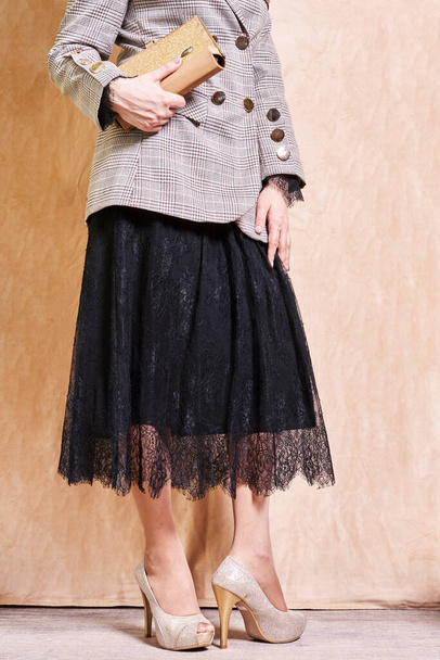 μια γυναίκα με φούστα και σακάκι που κρατά μια τσάντα με το ένα χέρι στο γοφό της ενώ στέκεται δίπλα στο άλλο - Φωτογραφία, εικόνα