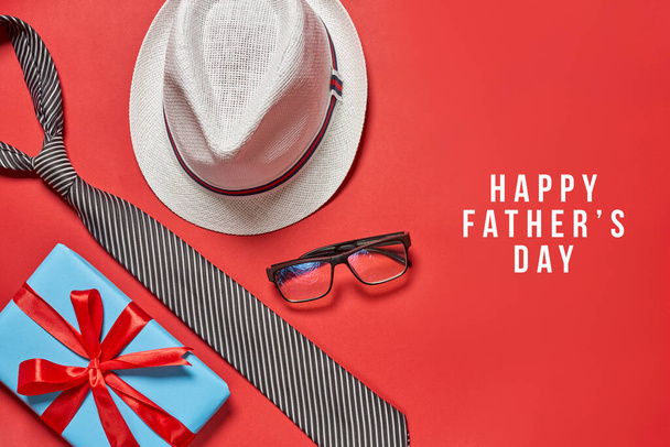 幸せな父親の日という言葉で赤い背景に男の帽子とネクタイと眼鏡 - 写真・画像