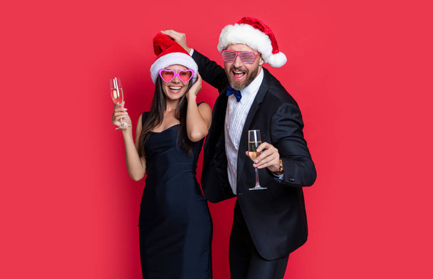 merry christmas to cheerful couple in studio. couple celebrate christmas. lets celebrate holiday. christmas couple celebrate with champagne isolated on red. celebrate christmas party with couple. - Foto, Imagem