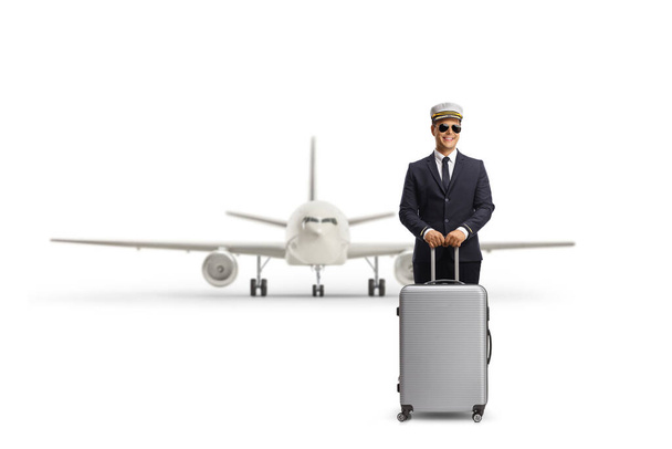 Young pilot standing with a suitcase in front of an airplane isolated on white background - Φωτογραφία, εικόνα