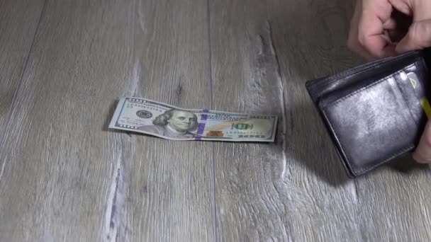 Bir adamın eli siyah deri bir cüzdandan dolar alıyor ve onları gri ahşap bir masaya koyuyor. 100 dolarlık banknotlar. - Video, Çekim