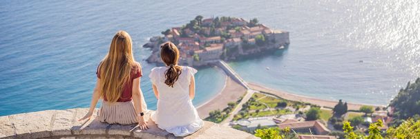 BANNER, LONG FORMAT Two Woman tourist on background of beautiful view of the island of St. Stephen, Sveti Stefan on the Budva Riviera, Budva, Montenegro. Travel to Montenegro concept. - Foto, afbeelding
