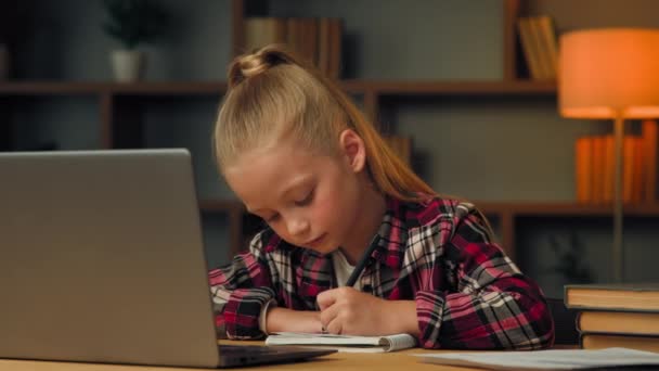 Кавказька дитина початкової школи мало розумна дівчинка-лялька вчиться онлайн з дзвінком до ноутбука на веб-конференції, навчаючись онлайн-уроку писати домашнє завдання на концепції домашньої освіти - Кадри, відео
