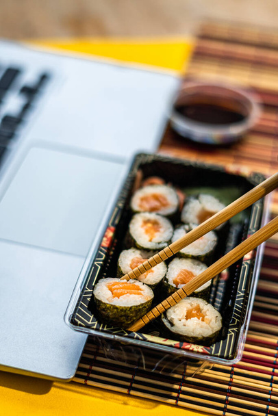 Sushi con salsa di soia accanto a un computer portatile, cibo da asporto asiatico - Foto, immagini