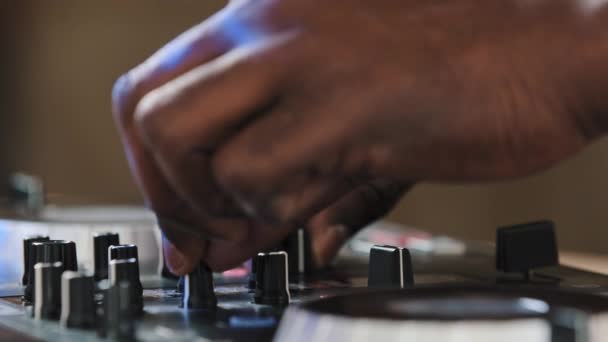 Zamknij męskie ręce afrykańskiego DJ-a grającego muzykę na imprezie nocnego klubu mieszającego taneczny rytm na mikserze tworzącego muzyczną energię na scenie festiwalowej twisty przyciski dodają efekty dźwiękowe - Materiał filmowy, wideo