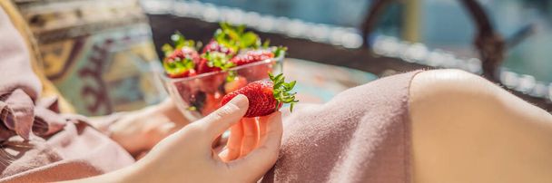 Portrait of gorgeous woman wearing beautiful dress sitting in a patio and eating strawberry. BANNER, LONG FORMAT - Foto, Bild