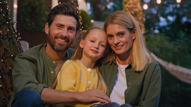 Family portrait happy Caucasian faces male female and kid woman bearded man and little girl father mother and child daughter outdoors smiling close up looking at camera in evening in camping backyard - Footage, Video