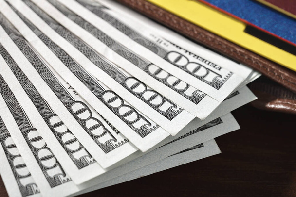 Κοντινό πλάνο των χαρτονομισμάτων των εκατό δολαρίων που προεξέχουν από ένα πορτοφόλι ξαπλωμένο σε ένα τραπέζι. - Φωτογραφία, εικόνα