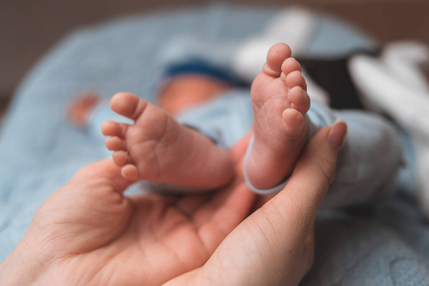 Primer plano, las manos de la madre sostienen las pequeñas piernas de un bebé recién nacido. - Foto, imagen