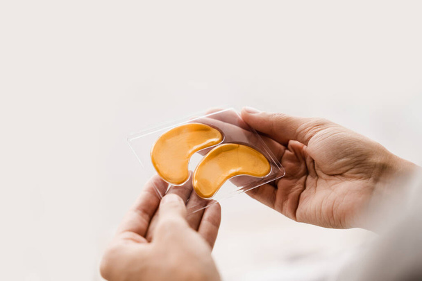 Close-up set of gold pathes for smooth out fine wrinkles, remove swelling or bags under the eyes. Golden hydrogel eye patches with peptides and hyaluronic acid in hands - Photo, Image