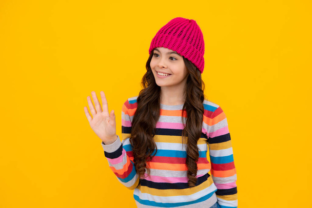 Beautiful winter kids portrait. Teenager girl posing with winter sweater and knit hat on yellow background. Happy teenager, positive and smiling emotions of teen girl - Foto, imagen
