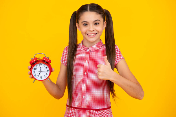 Boldog tinédzser lány tartja óra felett sárga háttér. Kora reggel, napirend. A gyerek ellenőrzi az időt. Ne késs el! Pontos gyerek riadóval. Határidő - Fotó, kép
