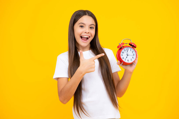 Excited teenager, glad amazed and overjoyed emotions. Child teenager girl with alrm clock isolated on yellow background. Time and deadline concept - Photo, image