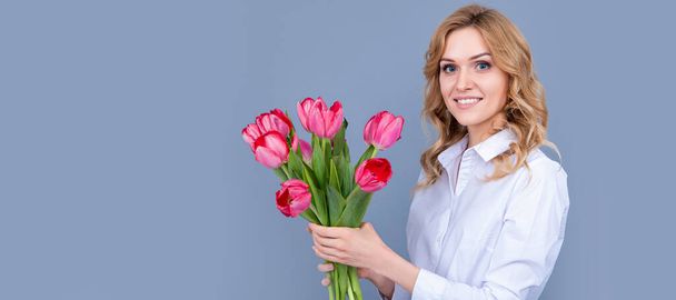 πρόσωπο της χαρούμενης νεαρής γυναίκας με ανοιξιάτικα λουλούδια τουλίπας σε γκρι φόντο. Γυναίκα απομονωμένο πορτρέτο πρόσωπο, πανό με μακιγιαρισμένο αντίγραφο χώρο - Φωτογραφία, εικόνα