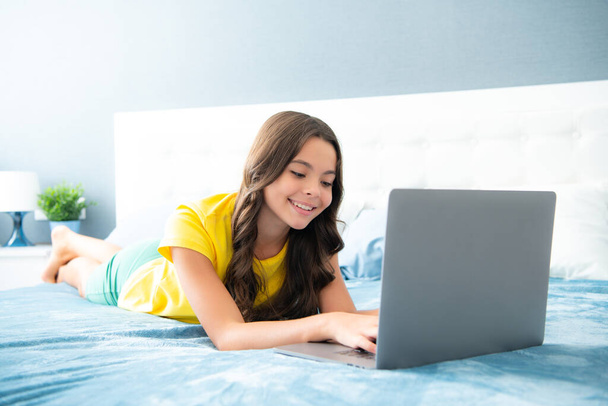 Teenage girl watching tv movie on laptop lying in bed. Teenager make video conference call online, learning online video course, relaxing in bedroom - Foto, imagen