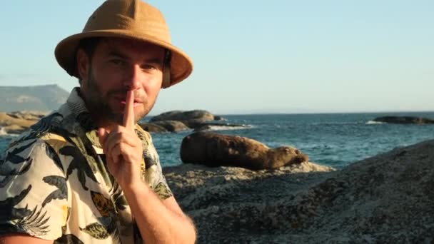 Männlicher Reisender mit Safari-Hut und Overalls blickt auf einen Seelöwen. Eine schöne Aufnahme einer kalifornischen Seelöwenrobbe, die die Sonnenstrahlen in Baja California genießt. eine Robbe sonnt sich in der Sonne, liegt auf einem Stein - Filmmaterial, Video