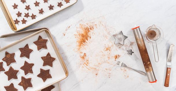 Düz yatıyordu. Kurabiye kesiciyle hamurdan yıldız şeklinde çikolatalı kraker kesmek.. - Fotoğraf, Görsel