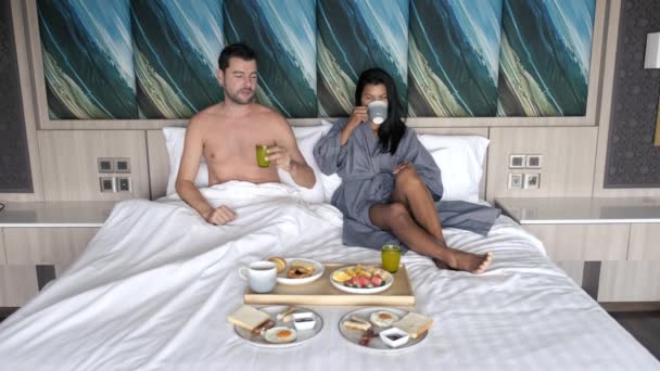 ベッドで朝食をとるカップル、白人男性とタイ人女性卵、クロワッサン、果物、コーヒーと寝室で朝食をとるタイ人女性 - 映像、動画