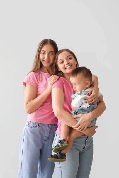 Happy lesbian couple with their little baby on grey background - Фото, зображення