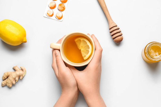 Woman with cup of tea, pills for sore throat, lemon, ginger and honey on light background - Photo, Image