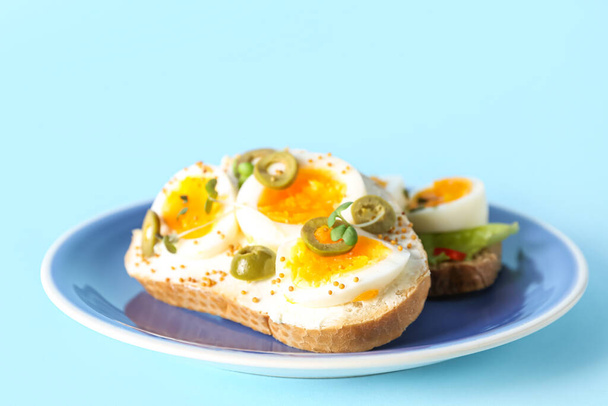 Placa de deliciosos brindis con huevo cocido y aceitunas sobre fondo de color - Foto, Imagen