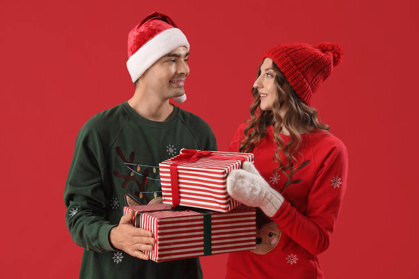 Νεαρό ζευγάρι ερωτευμένο με χριστουγεννιάτικα δώρα σε κόκκινο φόντο - Φωτογραφία, εικόνα