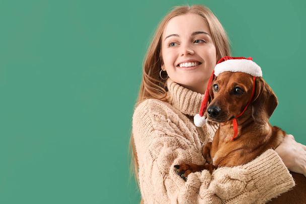 Jonge vrouw met teckel hond in Santa hoed op groene achtergrond, close-up - Foto, afbeelding