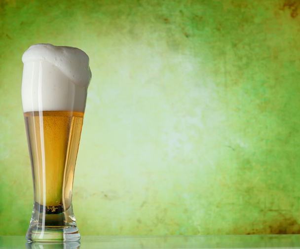 glas bier op een groene achtergrond - Foto, afbeelding