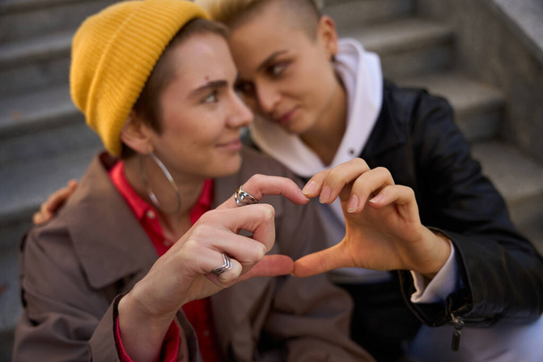 Young LGBT female couple holding hands in a heart shape, women settled down on the steps - Photo, Image