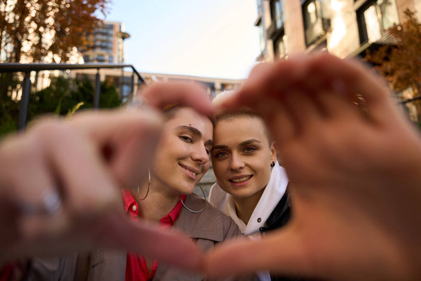 Young women hold their hands like heart, they are on a walk in the autumn city, they are a couple - Фото, зображення