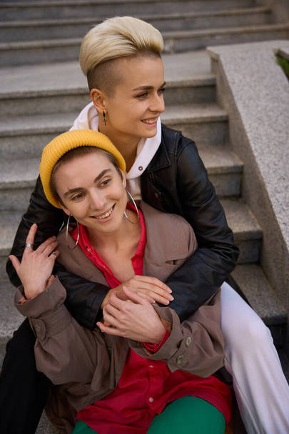 Smiling young women sit embracing on the steps, they are walking together in the city - Фото, зображення
