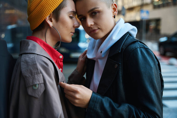 Two women stand against the wall of a large building, they gently touch each other, they are an LGBT couple - Fotó, kép