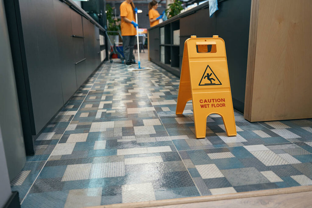 Warning sign Attention wet floor stands indoors on the floor, the cleaner washes the floor with a mop - Photo, Image