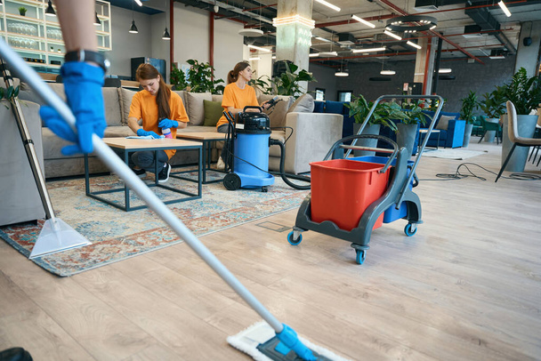 Reinigung im Coworking-Bereich: Arbeiter benutzen Staubsauger, Wischmopp und Eimer auf einem speziellen Wagen - Foto, Bild