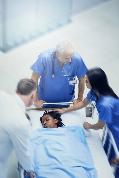 Ha bisogno di cure mediche immediate. un gruppo di medici che guardano un paziente su una barella in un corridoio ospedaliero - Foto, immagini