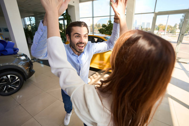 Joyful guy giving high five to his female companion at auto dealership - Foto, imagen