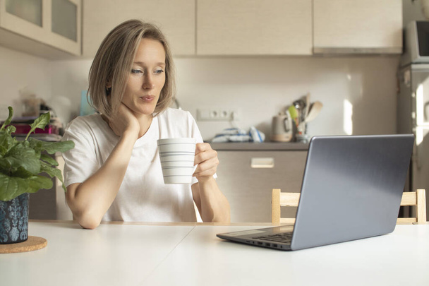 fiatal nő a konyhában egy bögre és egy laptop - Fotó, kép