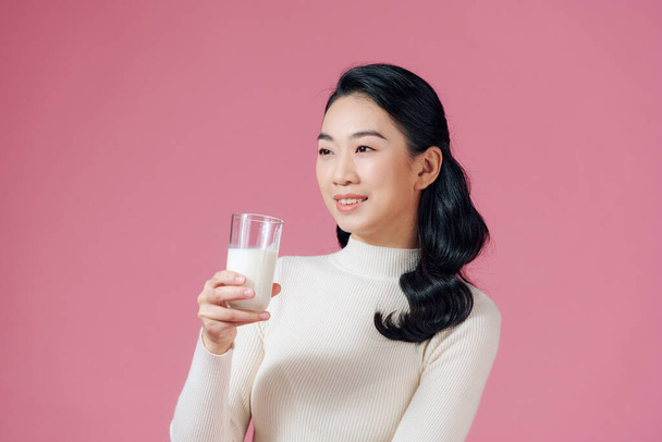 Portrait d'une jeune femme asiatique satisfaite buvant du lait à partir du verre isolé sur fond rose - Photo, image
