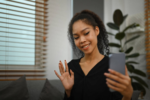 Cheerful young woman holding smartphone making video call to friends or relatives, enjoying pleasant conversation. - Foto, Bild
