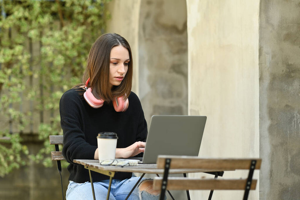 Заколдованная молодая женщина-фрилансер работает над онлайн-проектом на ноутбуке, сидя на открытом воздухе. - Фото, изображение