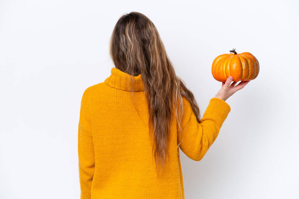 Young blonde woman holding a pumpkin isolated on white background in back position - Φωτογραφία, εικόνα