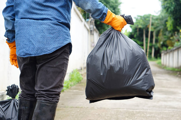 Closeup man holds black plastic bag that contains garbage inside. Concept : Waste management. Environment problems. Daily chores. Throw away rubbish. - 写真・画像
