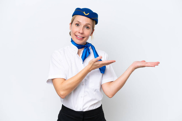 Uçaktaki sarışın hostes kadın, beyaz arka planda izole edilmiş, davet edilmek için ellerini yana uzatıyor. - Fotoğraf, Görsel