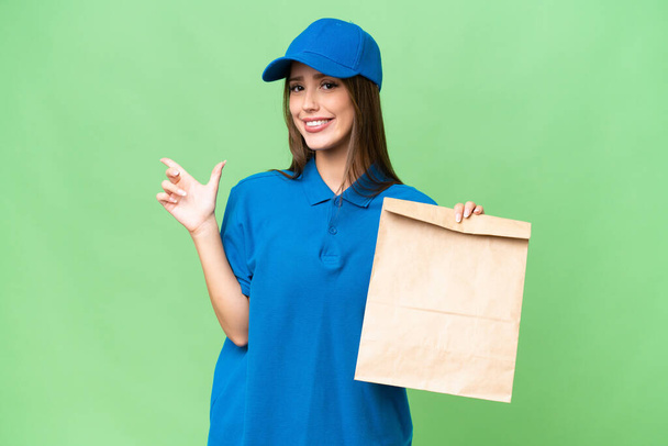 Jovem bela mulher caucasiana levando um saco de comida takeaway sobre fundo isolado apontando o dedo para o lado - Foto, Imagem
