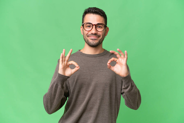 Mladý pohledný běloch muž přes izolované pozadí ukazující ok znamení se dvěma rukama - Fotografie, Obrázek