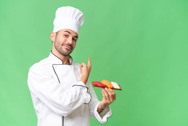 Jeune chef caucasien tenant un sushi sur fond isolé pointant vers l'arrière - Photo, image