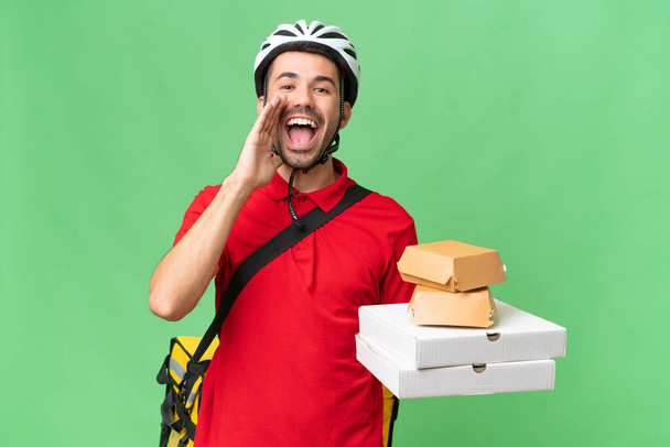 Young handsome caucasian man with thermal backpack and holding takeaway food over isolated background shouting with mouth wide open - Photo, Image